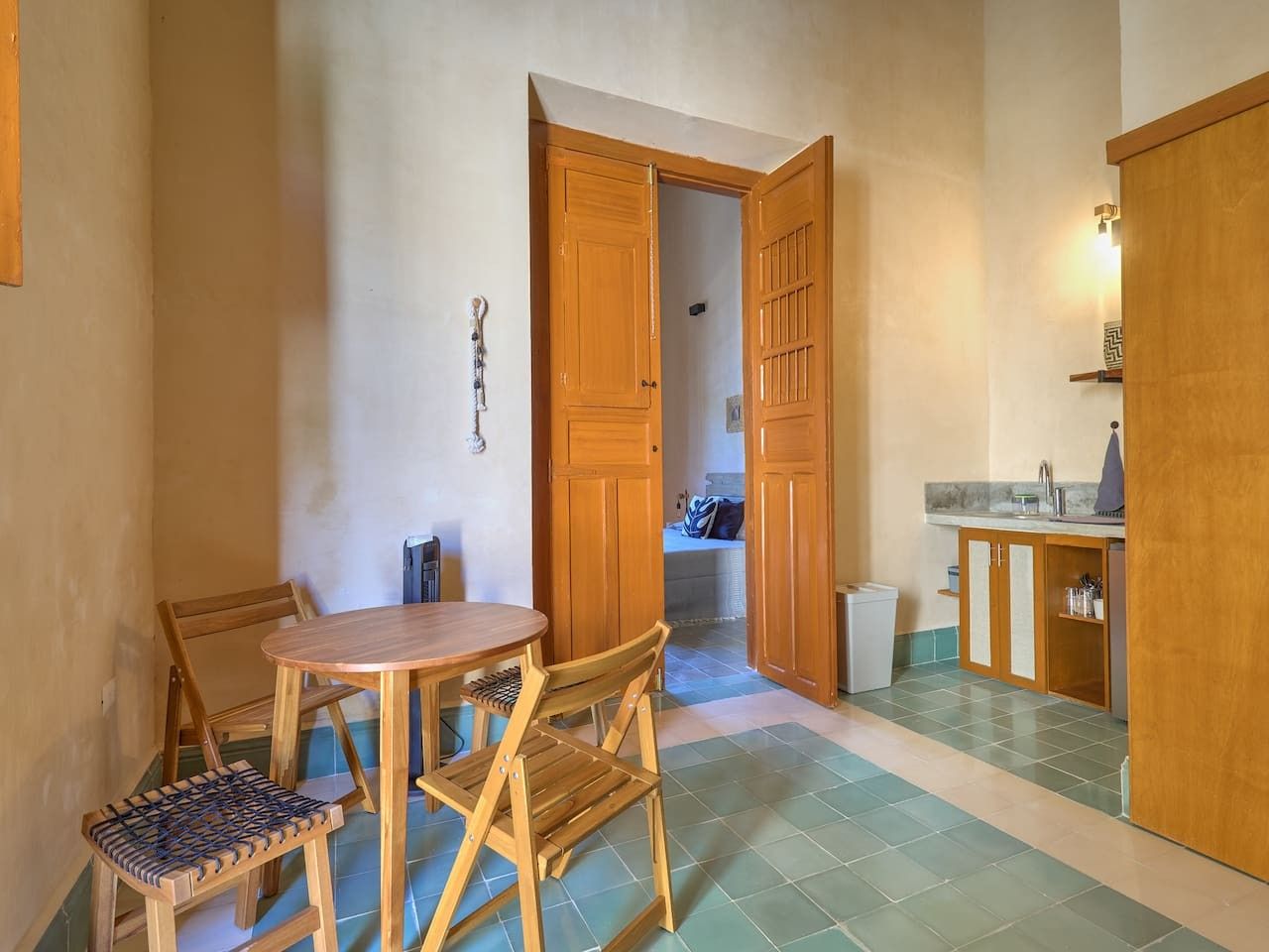 Una stanza con un tavolo e sedie in legno, un angolo cottura con pensili, e un corridoio che porta a un'altra stanza.