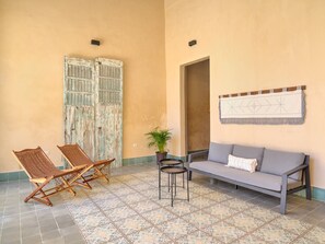 Quarto com sofá, duas cadeiras, uma mesinha e um vaso de planta.