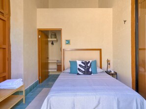 A bedroom with a bed, pillows, a nightstand, a lamp, and a wooden shelf with towels. - Studio w/private bathroom + pool / A+ Location (Merida)