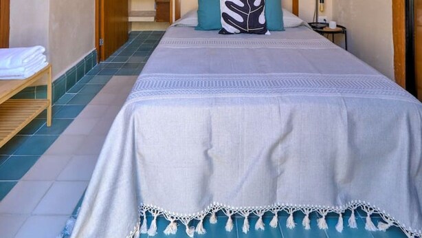 Ein Schlafzimmer mit einem Bett, einem Nachttisch, einer Lampe, einer Tür und einem kleinen Tisch mit einem Handtuch.