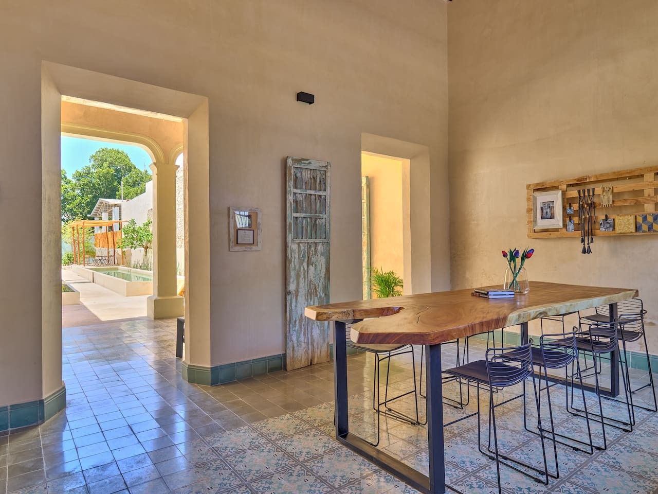 Un espace intérieur spacieux, avec une table en bois et des chaises en métal, une porte rustique et une vue sur une piscine extérieure.