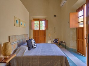 Une chambre à coucher comprenant un lit, une table de chevet, une lampe, une chaise, une petite table et une fenêtre donnant sur un beau paysage.