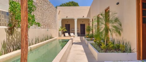 Un área de piscina con un camino accesible, sillas de descanso y un edificio de fachada de piedra.
