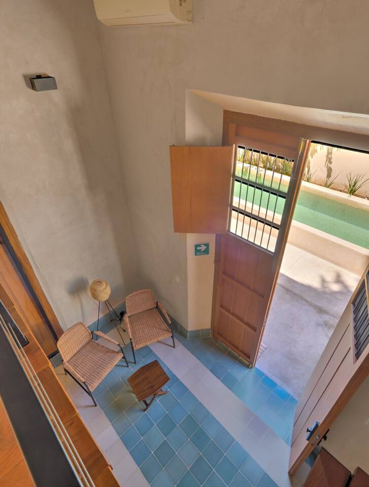 A room with a view of a swimming pool, a wooden door, a small table with a chair, and a lamp.