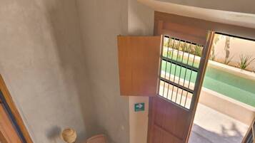 A room with a view of a swimming pool, a wooden door, a small table with a chair, and a lamp.