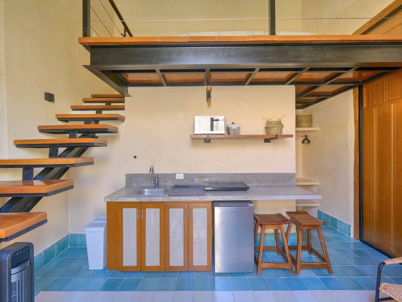 A compact kitchen with a built-in island, wooden stools, and a refrigerator.