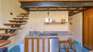 A compact kitchen with a built-in island, wooden stools, and a refrigerator.