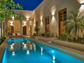Ein Swimmingpool mit klarer, blauer Wasseroberfläche, umgeben von einem Gebäude mit mehreren Fenstern und Türen, beleuchtet durch Außenbeleuchtung.