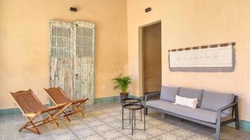 A room with a sofa, two chairs, a small table, a potted plant, and a wall-mounted artwork.