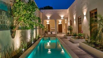 A swimming pool with a clear blue water surface, surrounded by a landscaped garden with various plants and a seating area with lounge chairs.