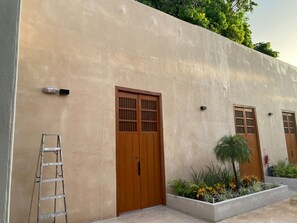 Ein Gebäude mit hellbeiger Fassade, zwei Holztüren mit Glasfeldern, einer Metallleiter und einem Pflanzkasten mit Pflanzen.