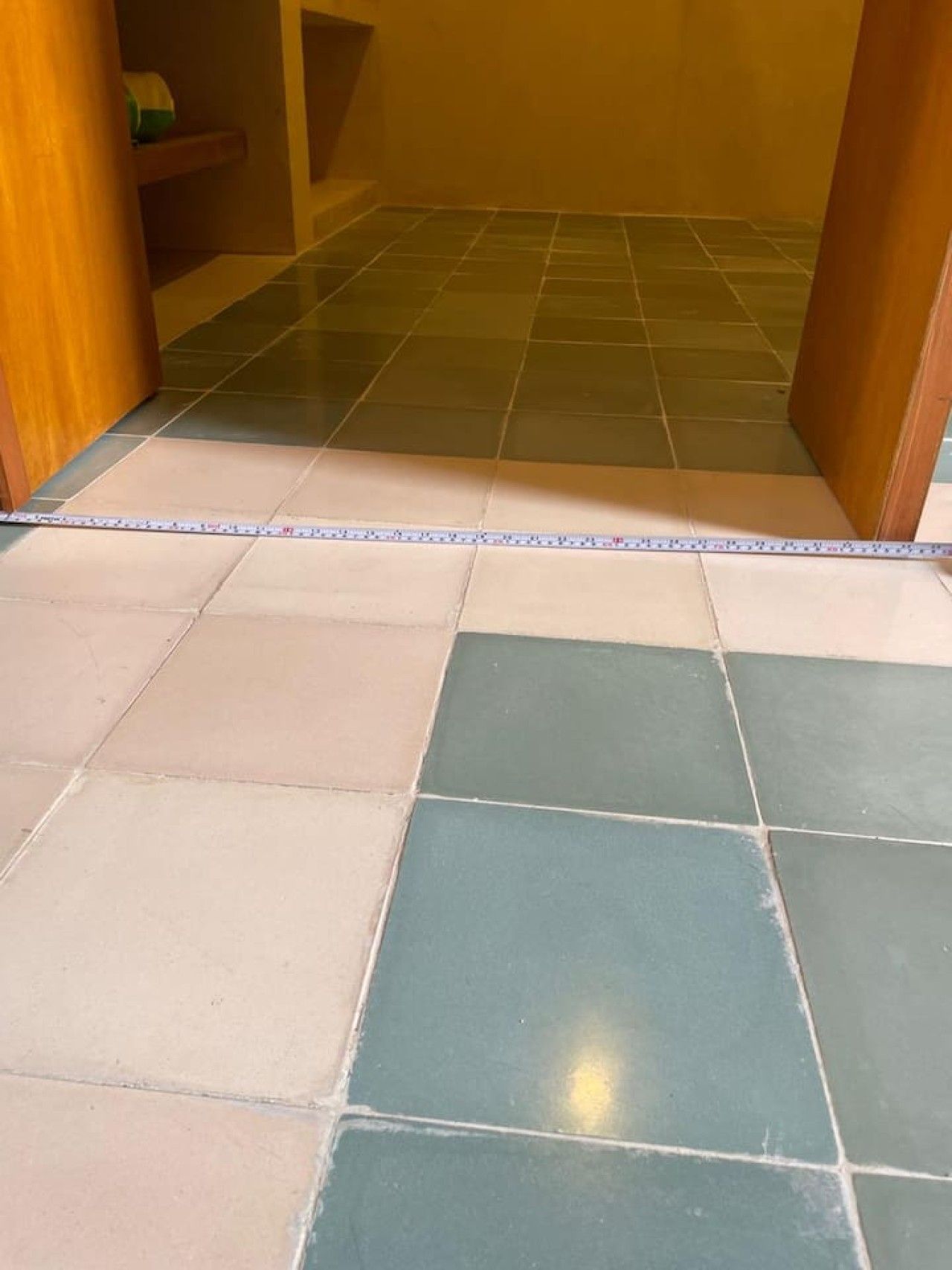 A hallway with a tiled floor, wooden walls, and a measuring tape on the floor.