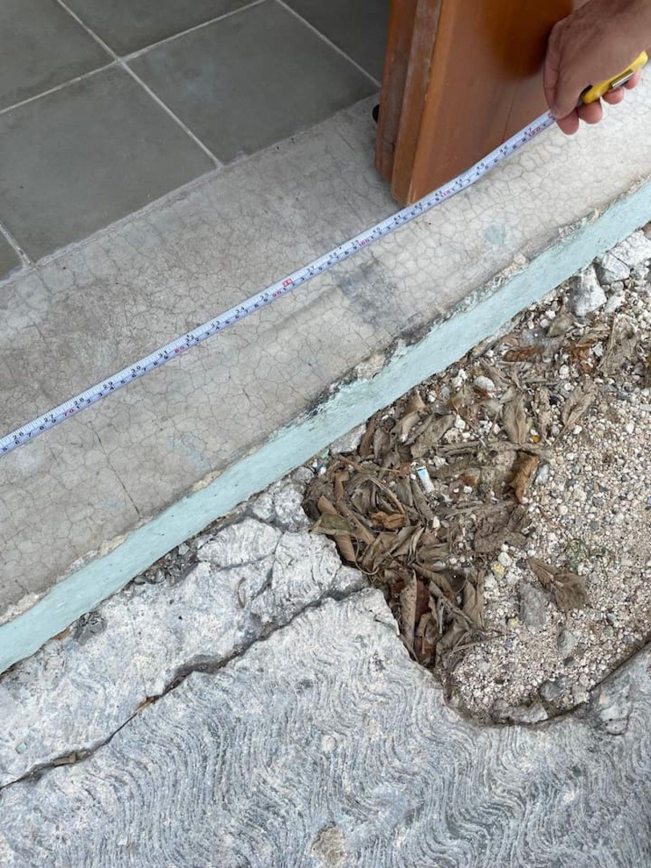 Una cinta mètrica estesa sobre un terra amb un dibuix de pedra rugosa i una estructura de fusta al fons.