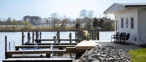 A lakeside dock with a wooden pier, a small building with outdoor seating, and a stone wall.