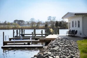 A lakeside dock with a wooden pier, a small building with outdoor seating, and a stone wall.
