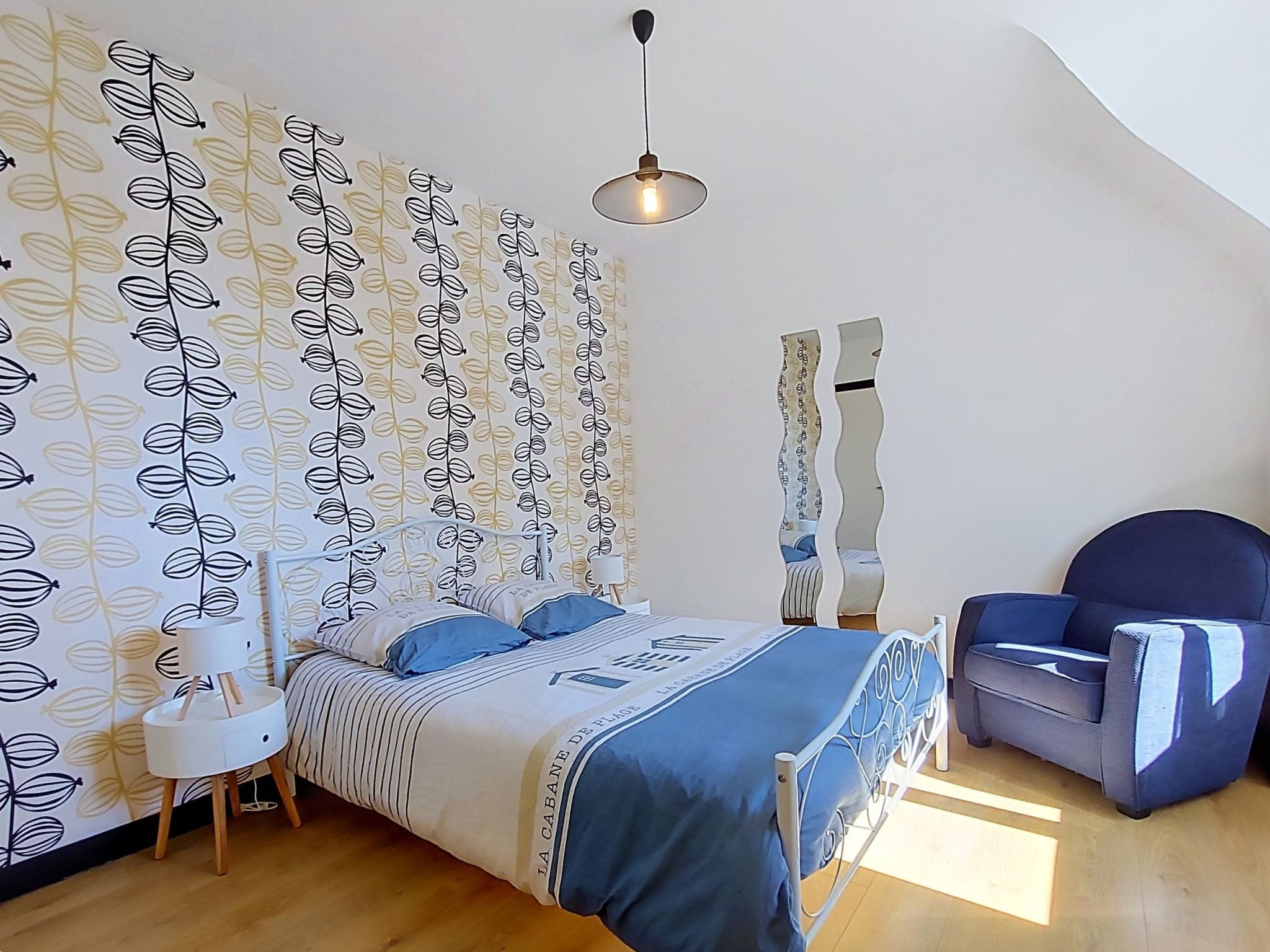 A bedroom with a bed, a chair, a lamp, and a wall with a leaf pattern.