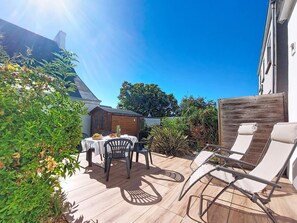 Una terrazza esterna con tavolo e sedie, circondata da piante e un recinto in legno.