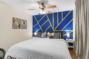 Ein Hotelzimmer mit einem Bett, einem Deckenventilator, einem Nachttisch und einer Wand mit geometrischen Mustern.