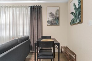 Ein Wohnzimmer mit einer Couch, einem Esstisch mit Stühlen, einer Holzbank und zwei gerahmten Pflanzenbildern an der Wand.