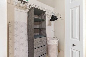 A storage unit with multiple shelves and hanging clothes racks, a white door, and a laundry basket with a label. - Your Ybor Base - WFH & Pet Friendly - Kitchenette (Tampa)