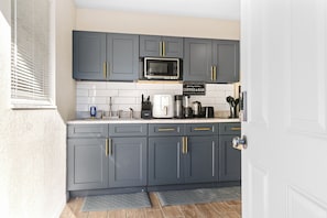 A kitchen with grey cabinets, a microwave, a coffee bar sign, and a sink. - Your Ybor Base - WFH & Pet Friendly - Kitchenette (Tampa)