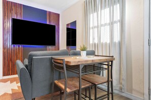 A modern living room with a flat-screen TV mounted on the wall, a grey sofa, a wooden coffee table, and a potted plant. - Your Ybor Base - WFH & Pet Friendly - Kitchenette (Tampa)