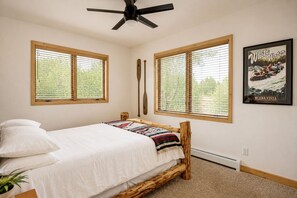 Ein Schlafzimmer mit einem Bett, zwei Fenstern, einem Deckenventilator und einem Poster an der Wand.