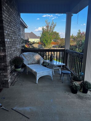 A covered patio with a wicker sofa, a small table, and a chair. - Get away from the crowds 3-bedroom house in charming Northport neighborhood (Northport)