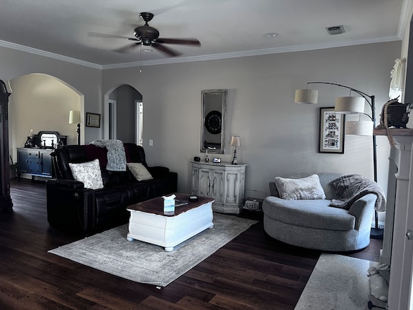 A living room with a ceiling fan, a dark leather sofa, a white side table, a grey armchair, and a wooden cabinet.