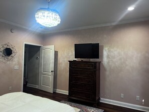 A bedroom with a bed, dresser, TV, and a chandelier.