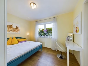 Quarto com cama, mesa de cabeceira, cadeira, janela com cortinas e luminária no teto.