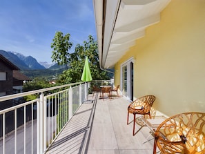 Uma varanda com vista para montanhas, uma mesa com cadeiras e um guarda-sol verde.