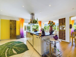 A modern kitchen with a central island, a wine rack, and a view of greenery outside.