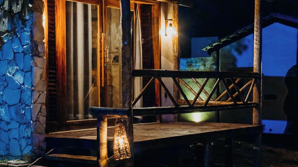 Una baita rustica in legno con veranda, muro in pietra e una piccola lampada.