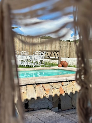 A swimming pool with a stone border, surrounded by a wooden fence and white outdoor furniture.