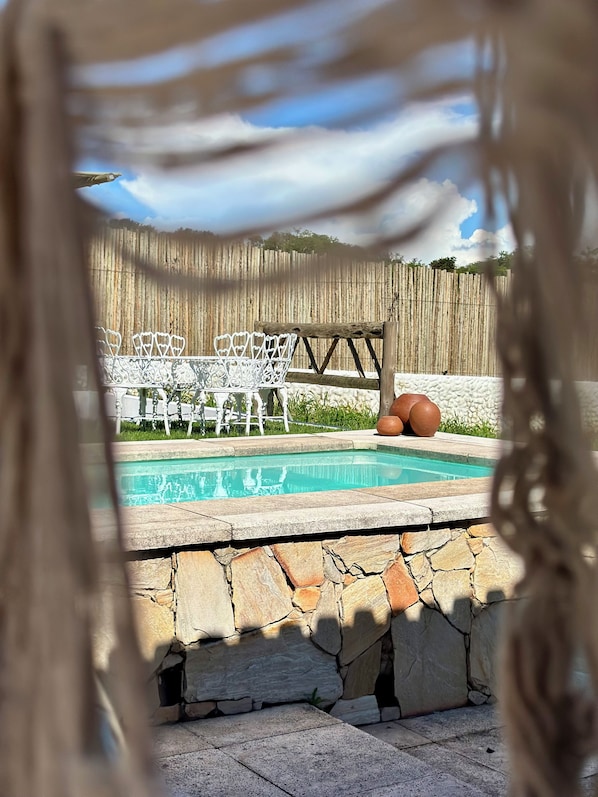 A swimming pool with a stone border, surrounded by a wooden fence and white outdoor furniture.