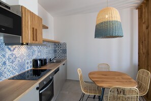 A modern kitchen with a wooden countertop, a built-in oven, and a sink. There is a dining table with four wicker chairs. A woven pendant light hangs above the table. - Villa in Agios Pavlos With Private Pool (Agios Vasileios)