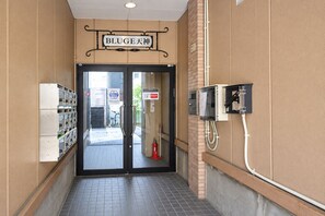 A hallway with a sign reading 'BLUGE 天神' above a double door, a fire extinguisher, and a utility box on the wall. - goom Monthly Nakasu BLUGE (Fukuoka City Chuoku Haruyoshi)