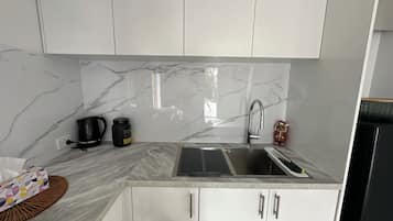 Een moderne keuken met witte kastjes, een marmeren spatwand, een spoelbak en een koffiezetapparaat.