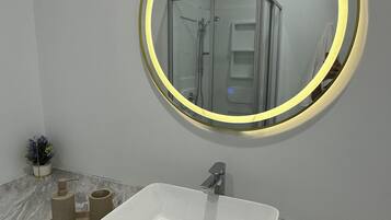 A bathroom with a white sink, a round mirror with a light, and a glass shower enclosure.