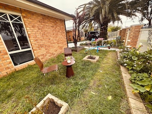 Una casa de ladrillo con jardín, un cortacésped azul y una pequeña mesa con una planta.