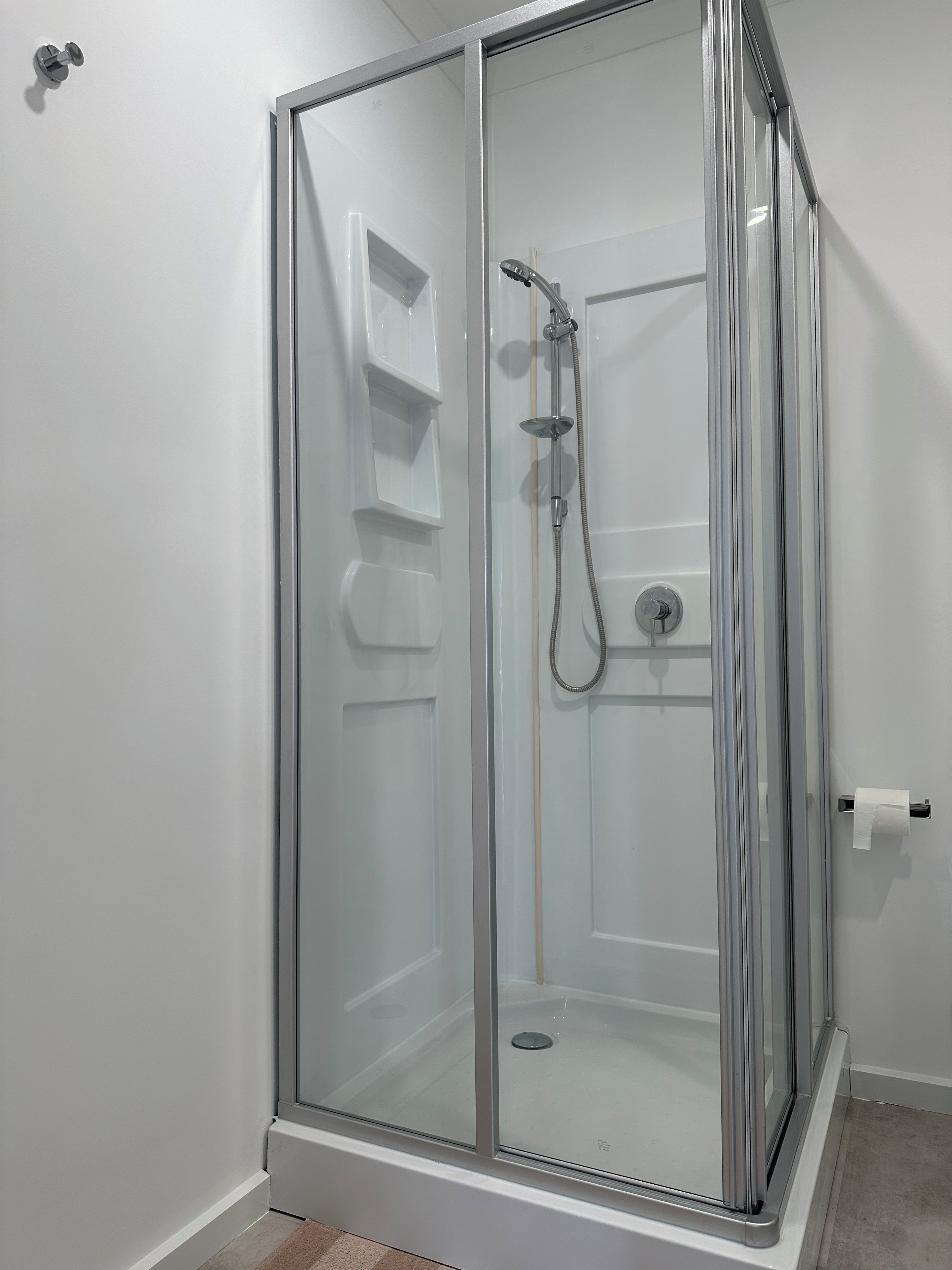 A glass-enclosed shower stall with a handheld showerhead and a wall-mounted faucet.
