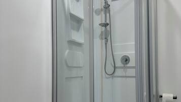 A glass-enclosed shower stall with a handheld showerhead and a wall-mounted faucet.