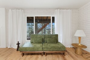 Ein Zimmer mit einem grünen Sofa, einem kleinen runden Tisch mit einer Lampe und Blick auf eine Holztreppe, die zu einem Balkon führt.