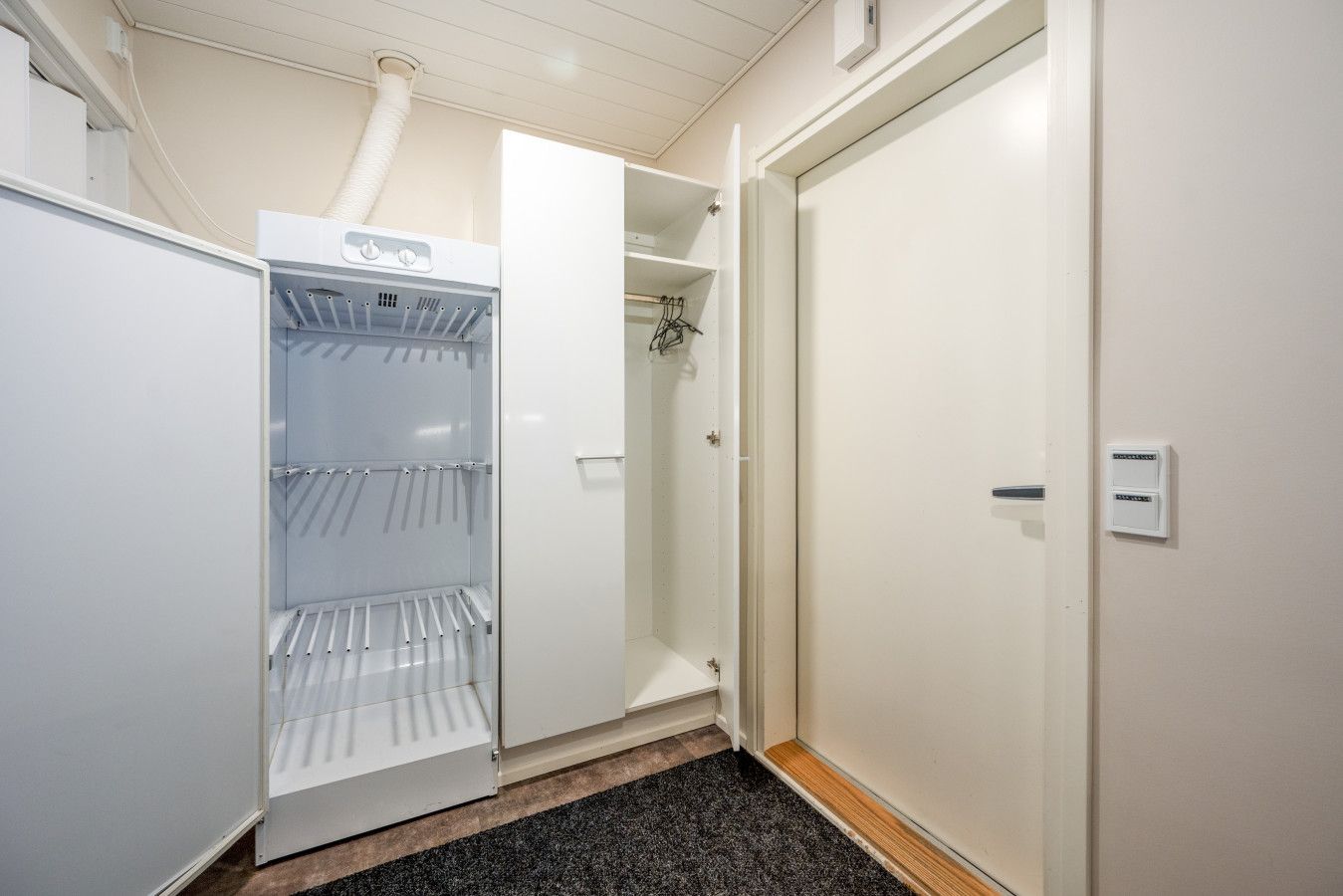 Ein Hotelzimmer mit eingebauter Minikühlschrank, einem Kleiderschrank und einer Tür mit Lichtschalter.