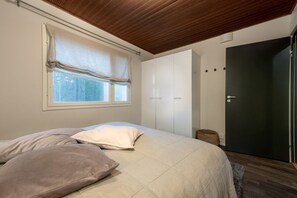 A bedroom with a bed, a window with curtains, a wardrobe, and a door.