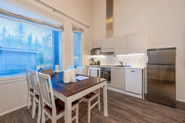 A modern kitchen with a dining table, chairs, a refrigerator, and a microwave.