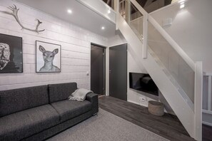 A modern living room with a grey sofa, a fireplace, and a staircase.