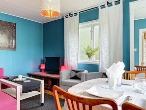 A room with a blue wall, a television, a dining table with chairs, and a window with curtains. - Villa Stensborg by Interhome (Östra Ryd)