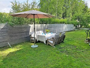 An outdoor dining area with a table set for four, a large umbrella, and a wooden fence in the background. - Villa Stensborg by Interhome (Östra Ryd)